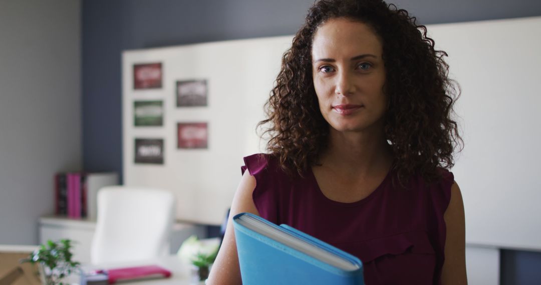 Confident Woman with Curly Hair Holding Folder in Modern Office - Free Images, Stock Photos and Pictures on Pikwizard.com