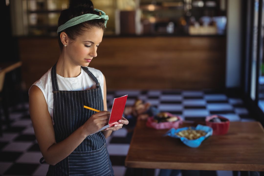 Baker in Pinstripe Apron Taking Notes Near Fresh Pastries