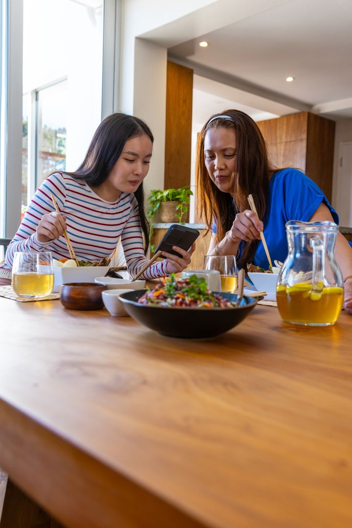 Mother and Daughter Enjoy Meal Together While Checking Smartphone
