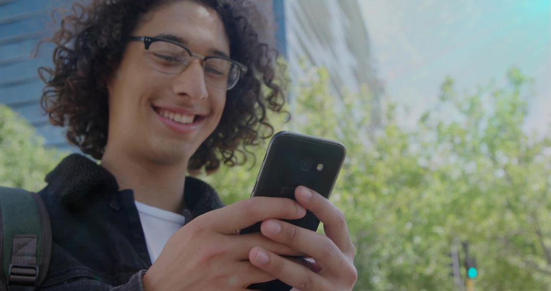 Young Man Smiling and Using Smartphone on City Street