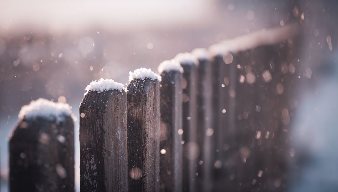 Weathered Wooden Picket Fence Wearing Snow Caps at Backlit Golden Hour with Bokeh