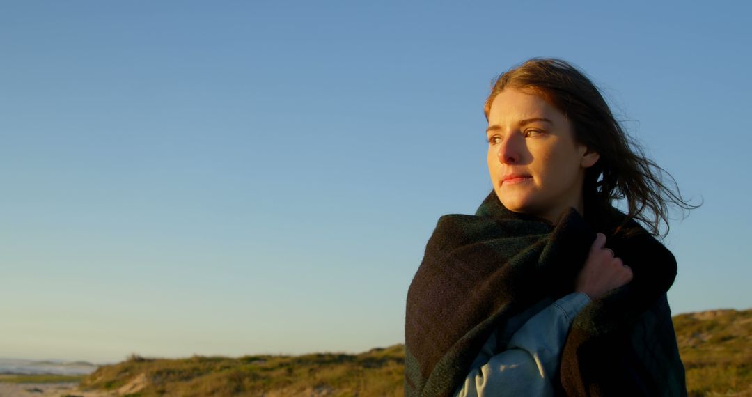 Thoughtful woman wrapped in blanket at sunset beach - Free Images, Stock Photos and Pictures on Pikwizard.com