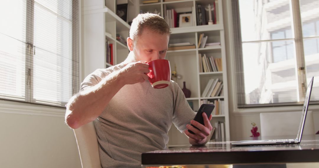 Young Adult Man Drinking Coffee While Using Smartphone at Desk - Free Images, Stock Photos and Pictures on Pikwizard.com