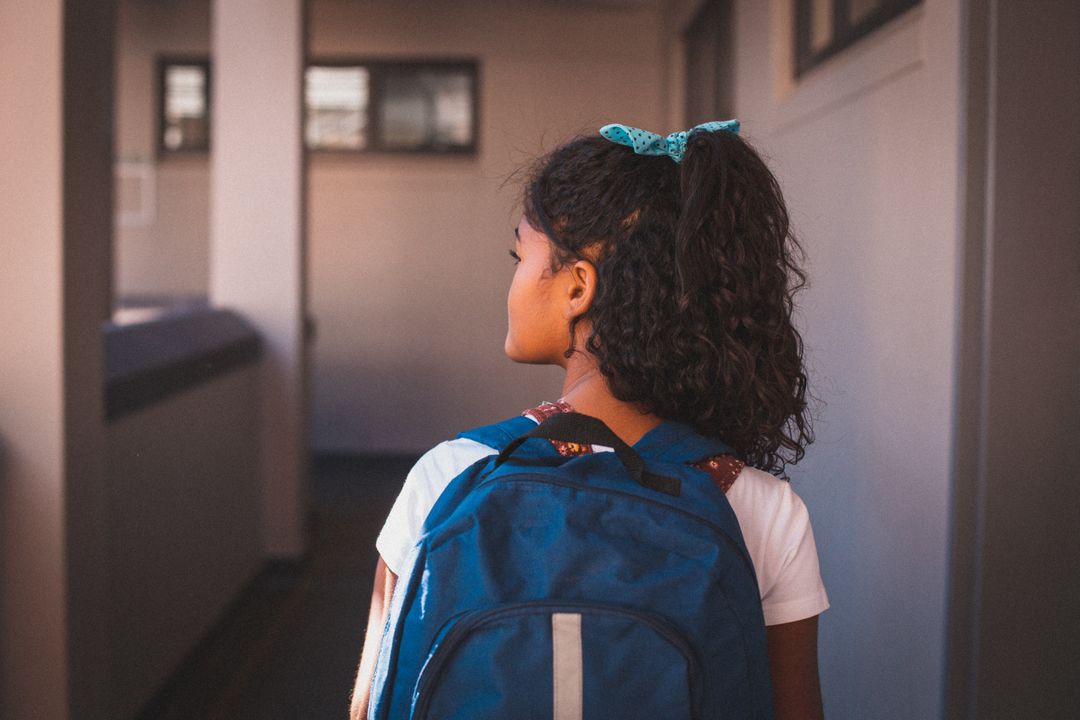 Rear view of biracial schoolgirl wearing backpack standing in school corridor - Free Images, Stock Photos and Pictures on Pikwizard.com