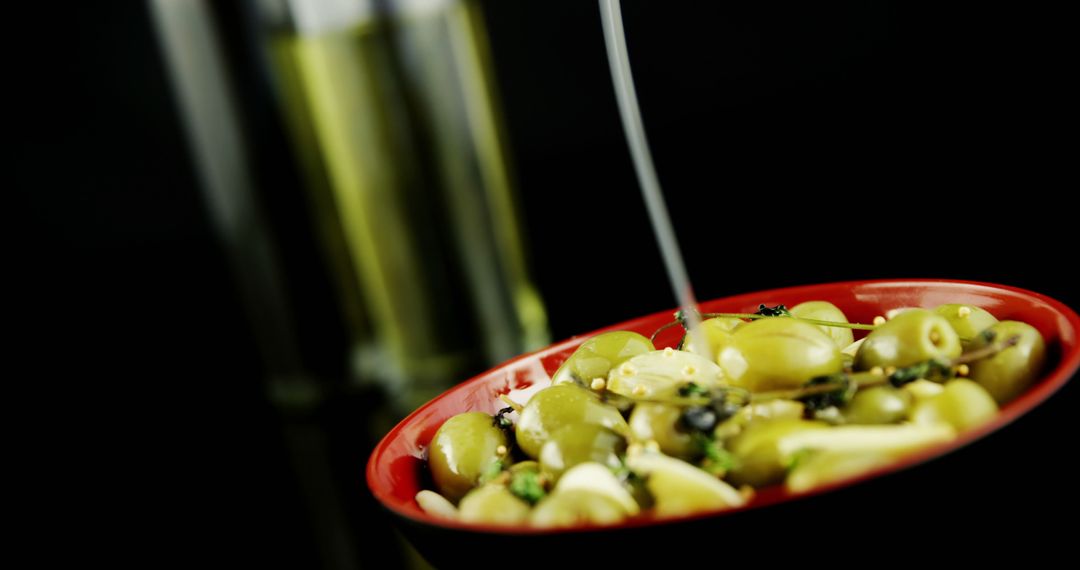 Pouring Olive Oil Over Green Olives in Red Bowl on Black Background - Free Images, Stock Photos and Pictures on Pikwizard.com