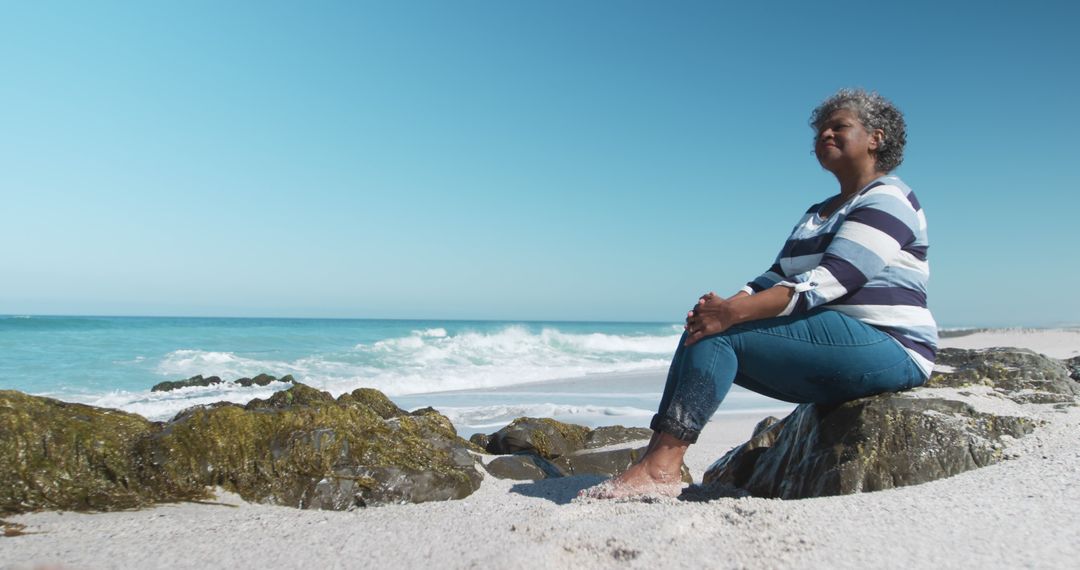 Senior Woman Sitting on Rocky Beach Enjoying Ocean View - Free Images, Stock Photos and Pictures on Pikwizard.com