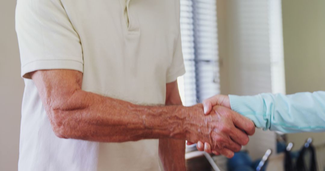 Elderly man in white shirt shaking hands with younger person indoors - Free Images, Stock Photos and Pictures on Pikwizard.com