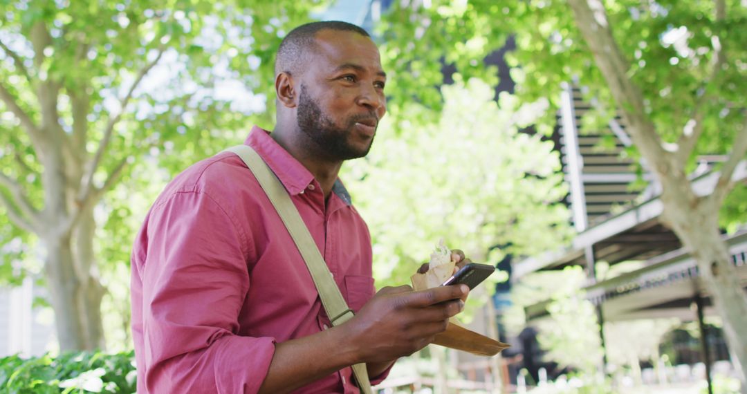 Smiling Man Enjoying Lunch in Urban Park Using Smartphone
