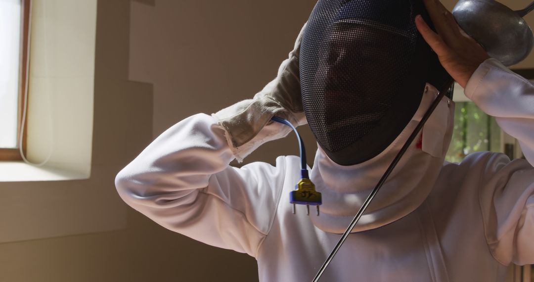 Fencer adjusting mask before practice in well-lit room - Free Images, Stock Photos and Pictures on Pikwizard.com