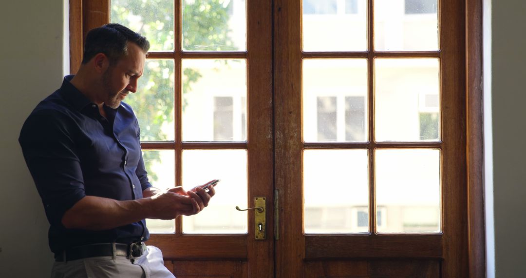 Businessman Standing by Window Using Smartphone - Free Images, Stock Photos and Pictures on Pikwizard.com