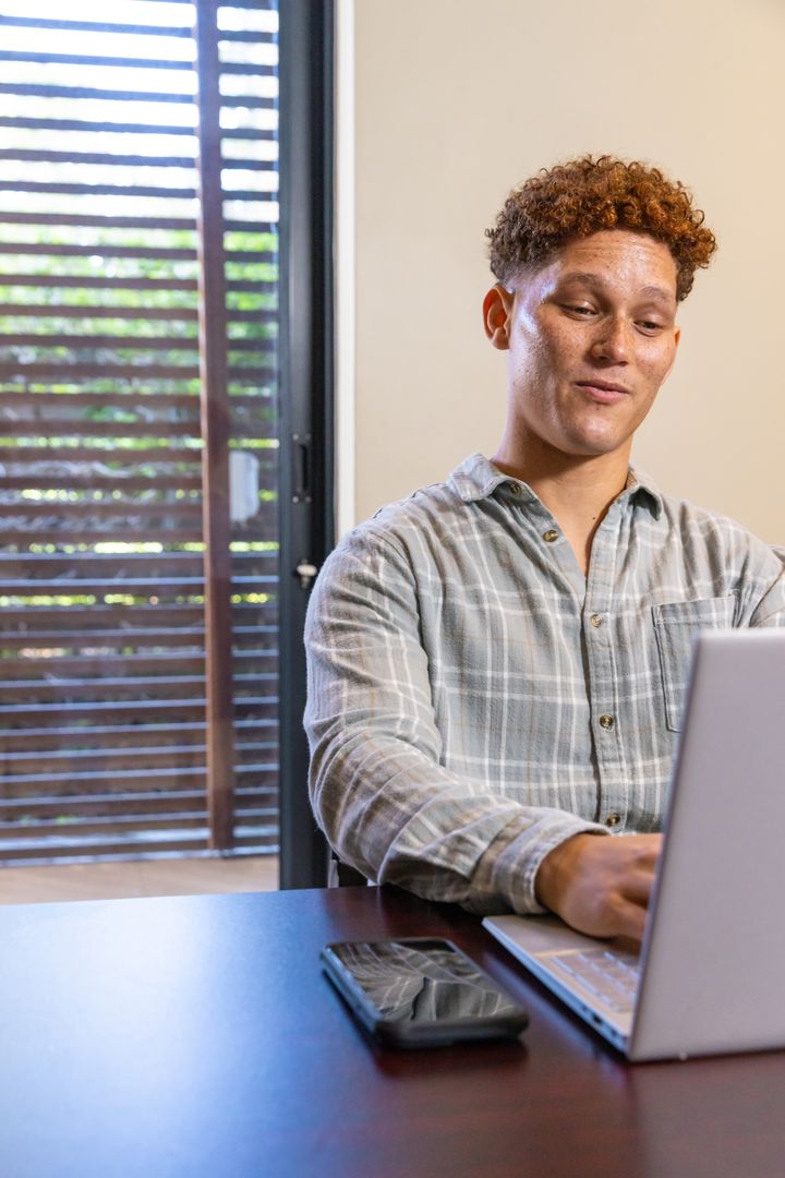 Man Working on Laptop at Modern Home Office Near Window