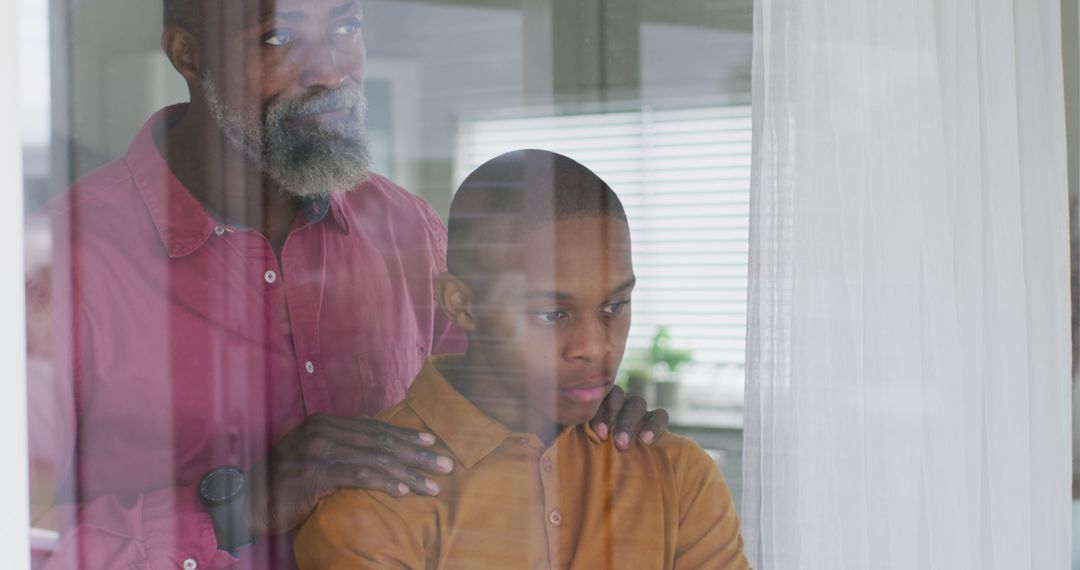 Supportive father consoling sad teenage son by window at home - Free Images, Stock Photos and Pictures on Pikwizard.com