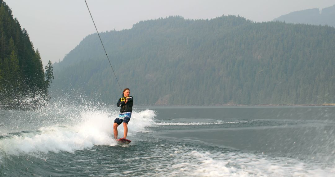 Young Man Wakeboarding on Lake Surrounded by Forested Mountains - Free Images, Stock Photos and Pictures on Pikwizard.com