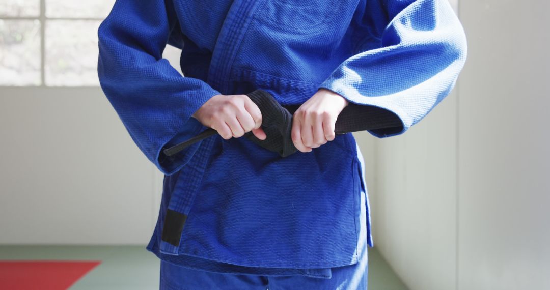 Martial Artist Tightening Black Belt in Blue Gi Uniform - Free Images, Stock Photos and Pictures on Pikwizard.com