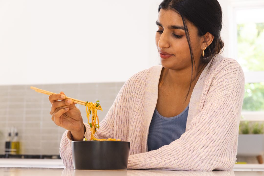 Woman Enjoying Noodle Meal with Chopsticks in Modern Kitchen