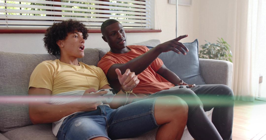 Friends playing video games on sofa at home, competing with controllers in cozy living room