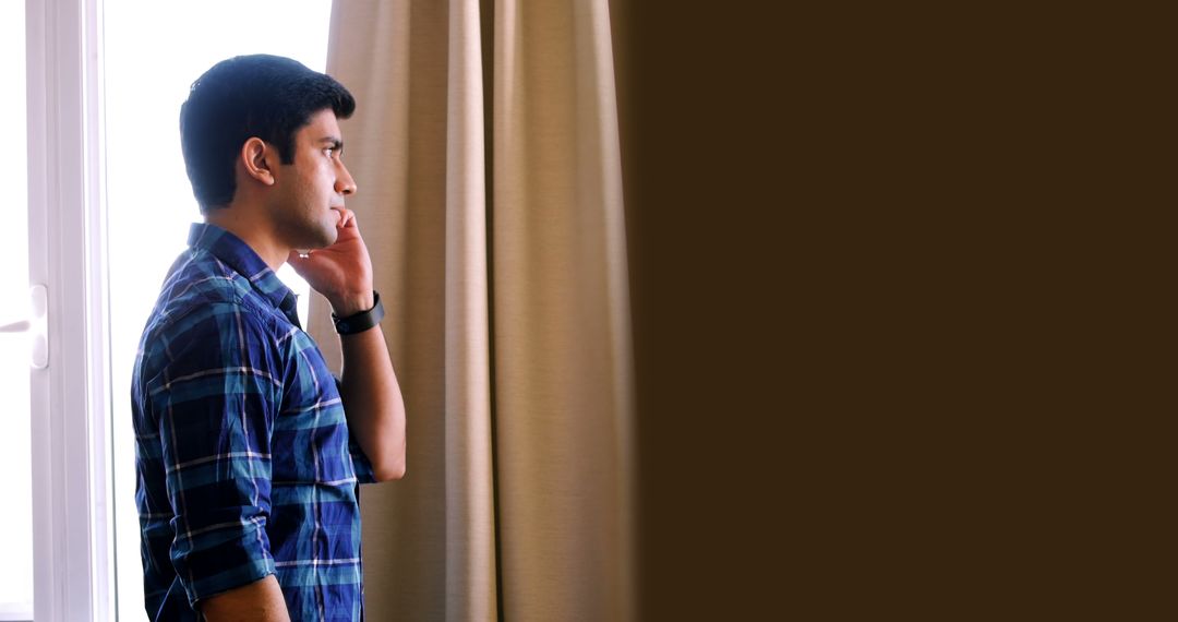 Young Man Talking on Phone by Window in Home Office Environment - Free Images, Stock Photos and Pictures on Pikwizard.com