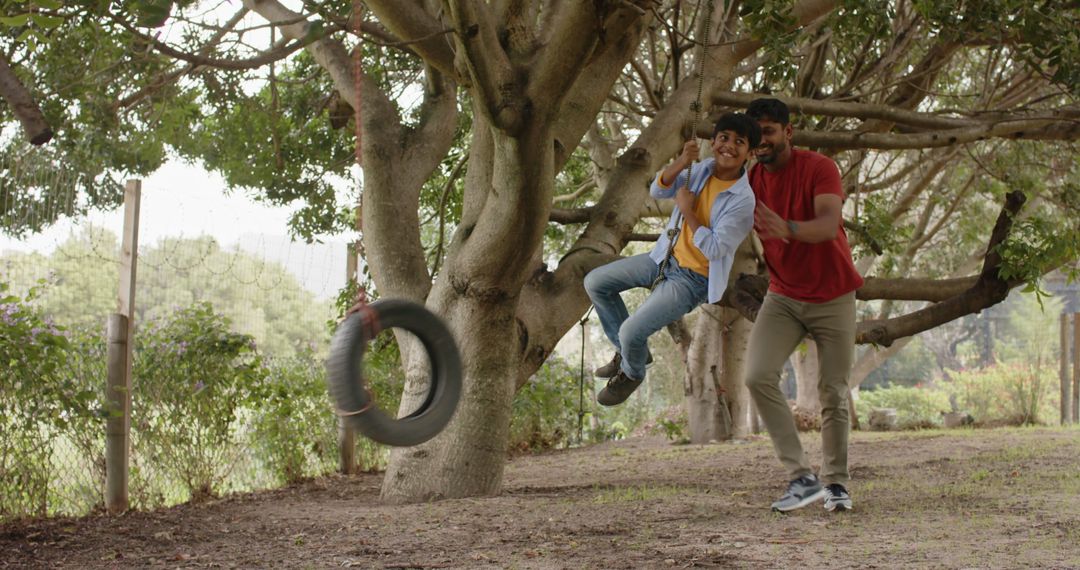 Father Pushing Son on Tire Swing in Shaded Garden