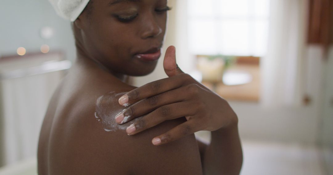 Portrait of african american attractive woman applying body balm in bathroom - Free Images, Stock Photos and Pictures on Pikwizard.com
