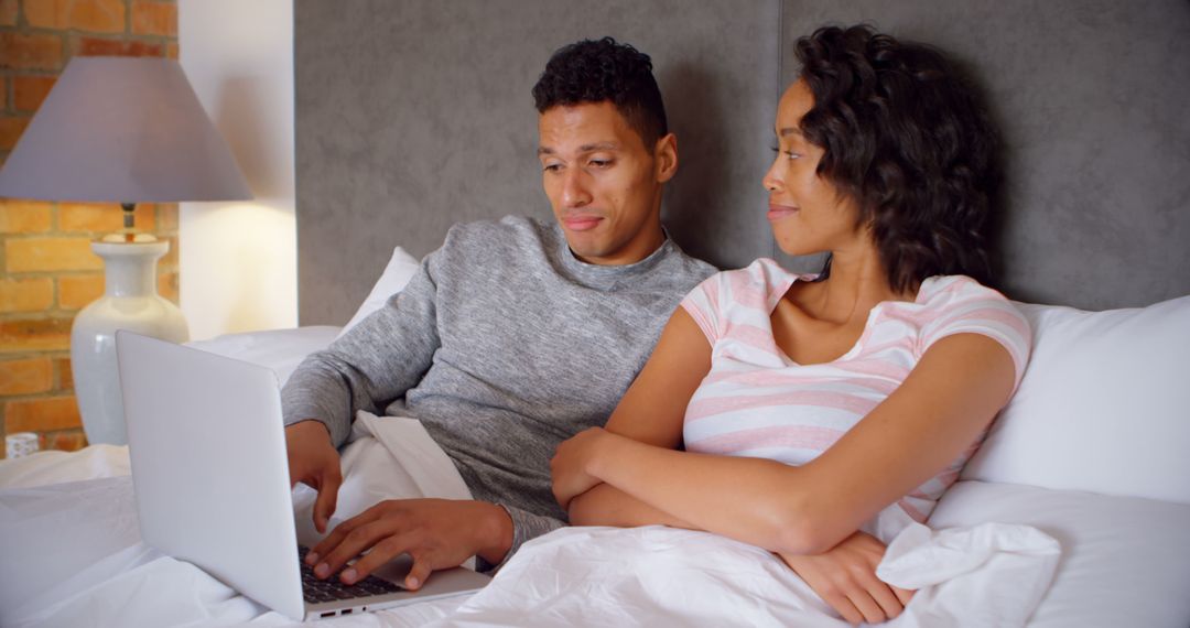 Couple Relaxing in Bed with Laptop Browsing Content Together