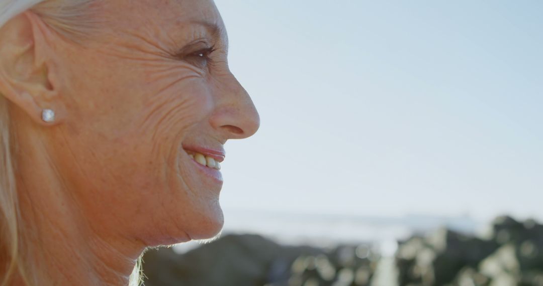 Older woman smiling outdoors with coastal rocks in background - Free Images, Stock Photos and Pictures on Pikwizard.com