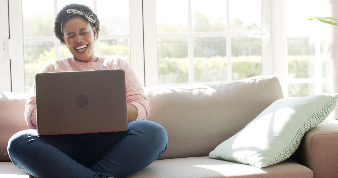 Laughing woman using laptop on sofa at home