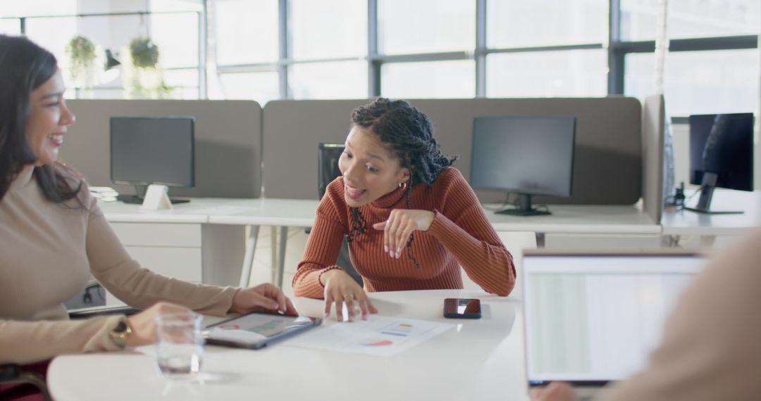 Diverse team collaborating and reviewing charts on tablet in modern open office workspace