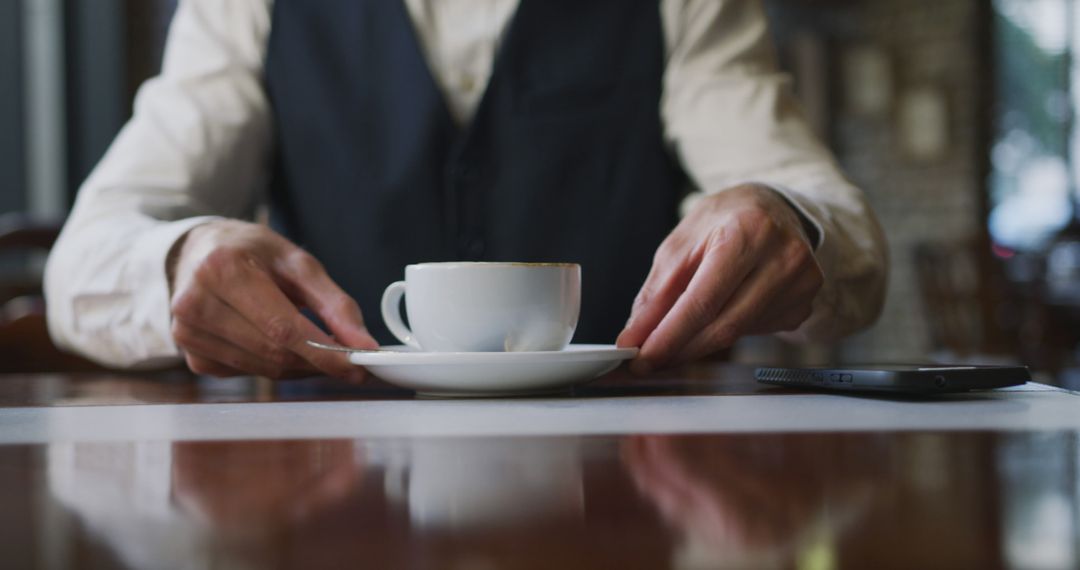 Man in vest holding coffee cup on saucer in cafe - Free Images, Stock Photos and Pictures on Pikwizard.com