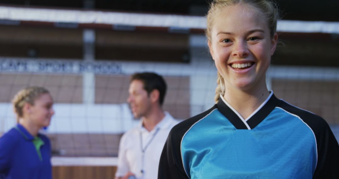 Teen Volleyball Player Smiling in Gym with Coach and Teammate in Background - Free Images, Stock Photos and Pictures on Pikwizard.com