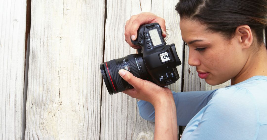 Female Photographer Adjusting Camera Against Wooden Background - Free Images, Stock Photos and Pictures on Pikwizard.com