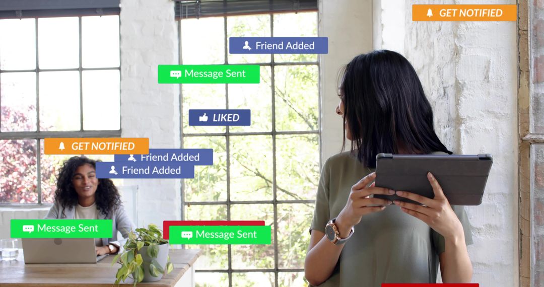 Woman Checking Tablet While Colleague Working on Laptop with Floating Social Alerts in Loft