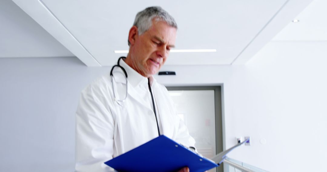 Senior Doctor Reviewing Medical File in Modern Hospital Corridor - Free Images, Stock Photos and Pictures on Pikwizard.com