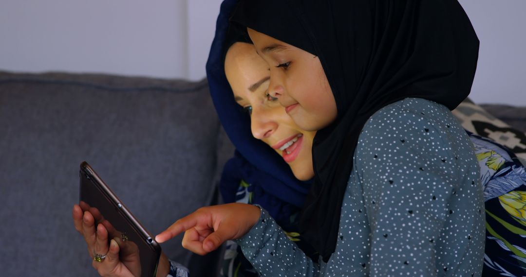 Mother and Daughter in Hijabs Enjoying Tablet Together on Sofa - Free Images, Stock Photos and Pictures on Pikwizard.com