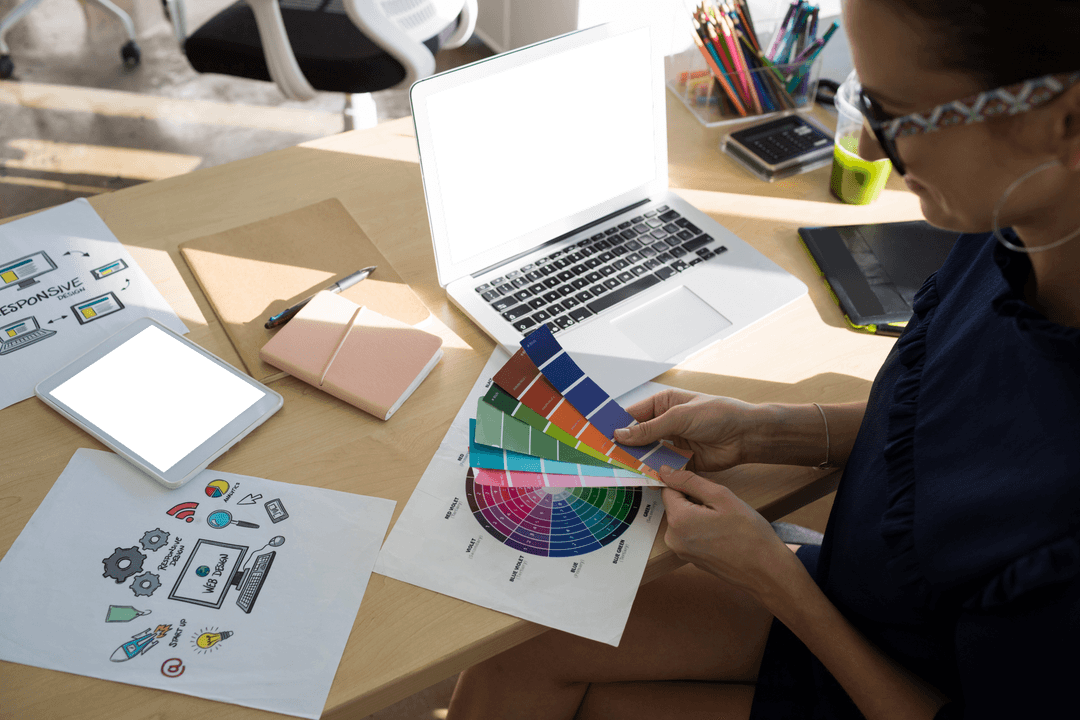 Female Designer Holding Color Swatch at Office Desk with Tech Devices