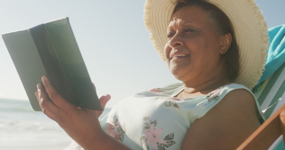 Smiling Senior Woman Reading Book on Beach in Sunshine - Free Images, Stock Photos and Pictures on Pikwizard.com