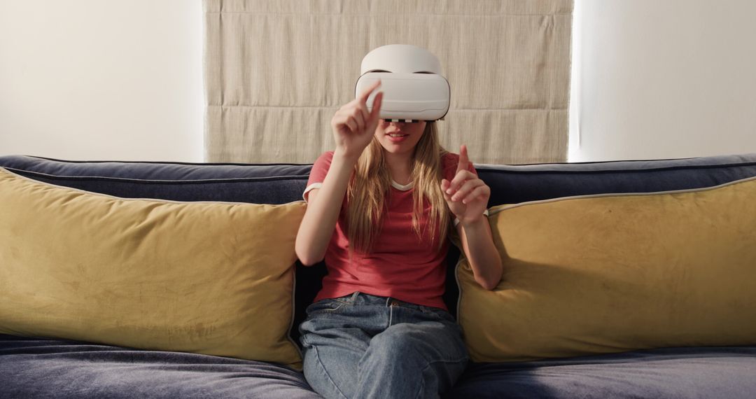 Young woman experiencing virtual reality on couch wearing white VR headset and gesturing