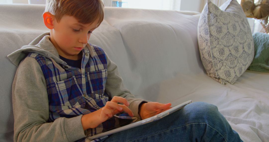 Young Boy Using Tablet on Sofa in Cozy Living Room - Free Images, Stock Photos and Pictures on Pikwizard.com