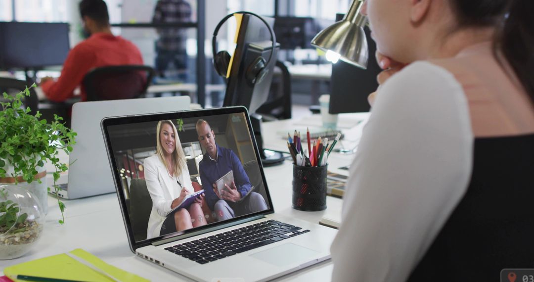 Female Employee Joining Virtual Meeting on Laptop in Open-Plan Office Workspace