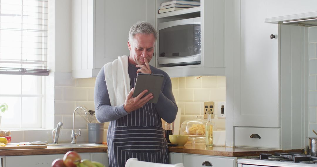 Mature Man Using Tablet in Modern Kitchen While Cooking - Free Images, Stock Photos and Pictures on Pikwizard.com