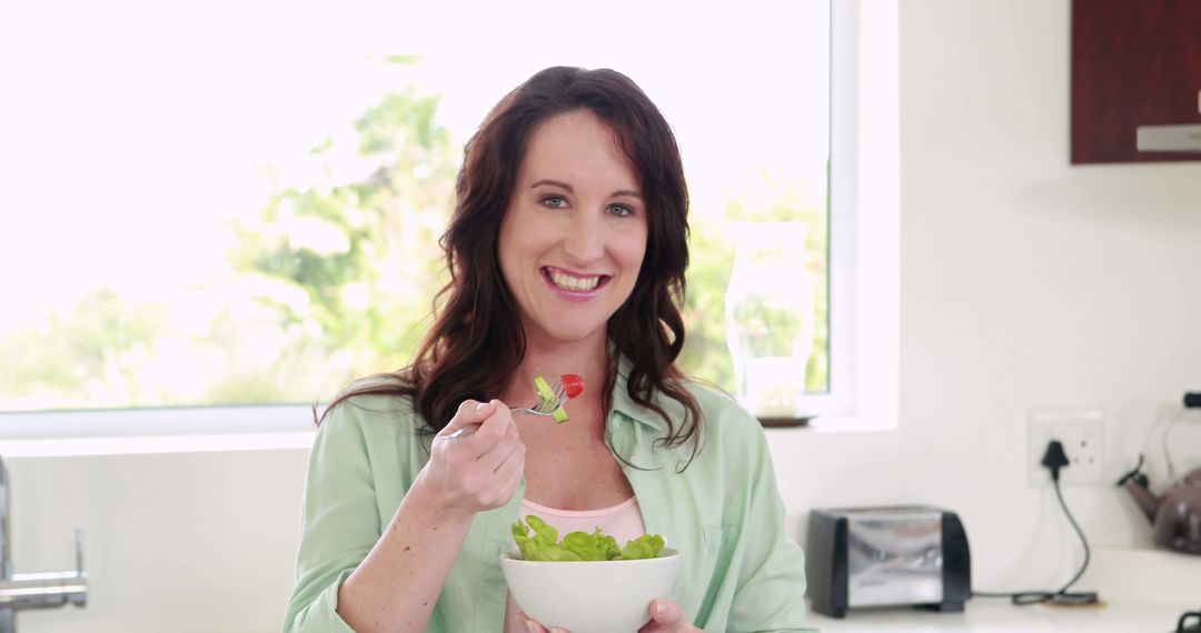 Happy Woman Eating Fresh Salad in Bright Kitchen - Free Images, Stock Photos and Pictures on Pikwizard.com