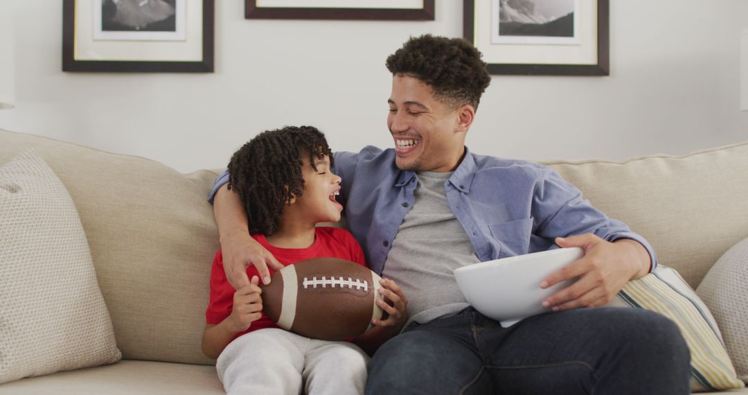 Father and Son Smiling on Couch with Football and Bowl Snacks - Free Images, Stock Photos and Pictures on Pikwizard.com