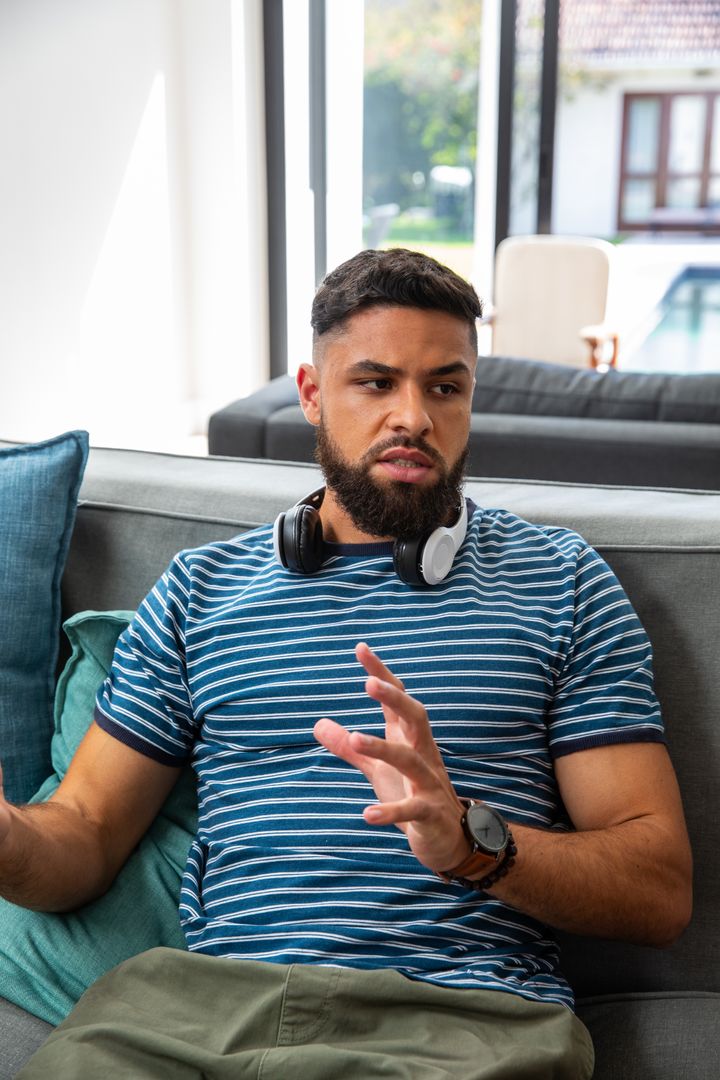 Man Gesturing on Couch with Headphones in Modern Living Room