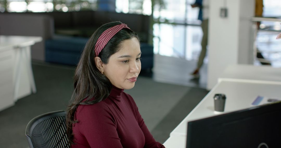 Hispanic professional woman typing at desk in modern coworking space, focused productivity