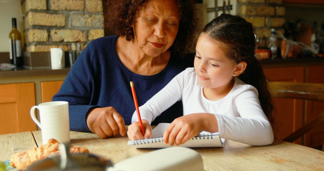 Affectionate Grandma Helping Granddaughter With Homework at Kitchen Table - Free Images, Stock Photos and Pictures on Pikwizard.com