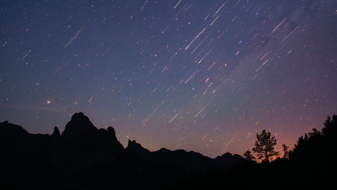 Startrails streaking over jagged mountain ridge with Milky Way and silhouetted tree