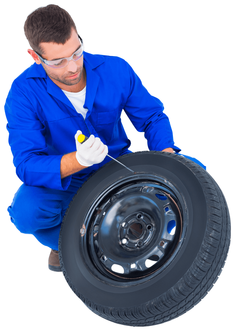 Mechanic in Blue Coveralls Kneeling with Tire Transparent Background