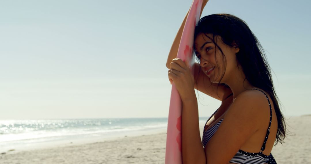Young biracial woman holds a surfboard on a sunny beach - Free Images, Stock Photos and Pictures on Pikwizard.com
