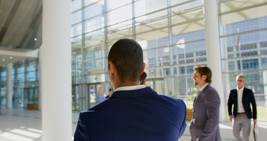 Rear View of Businessman in Modern Lobby on Mobile Phone