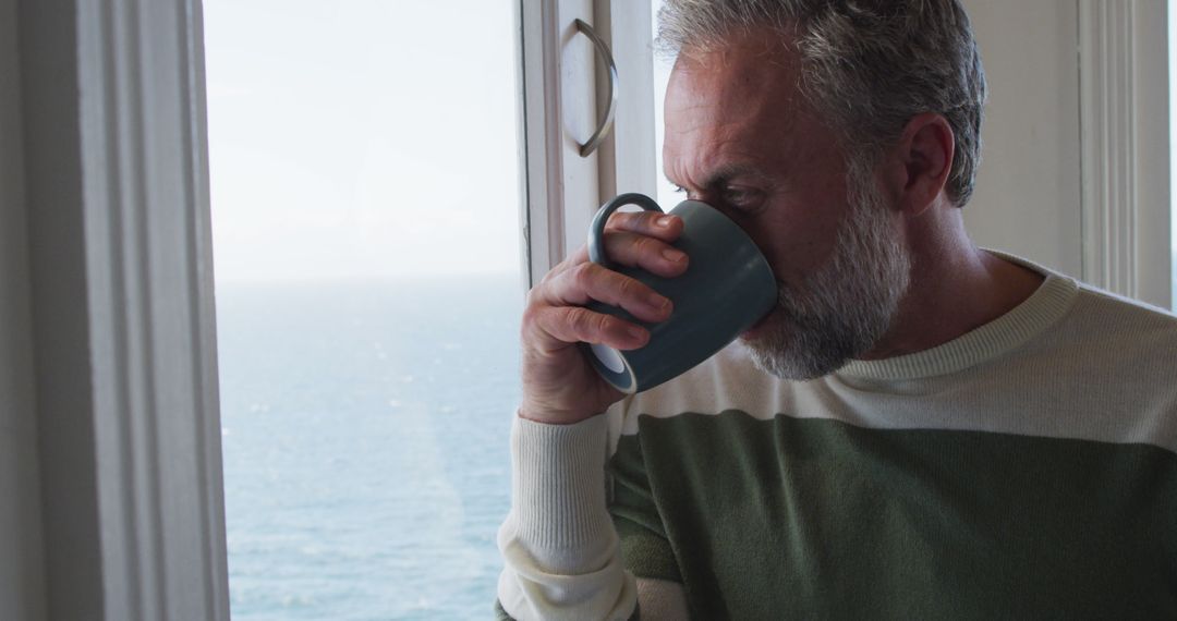 Middle-aged man enjoying hot drink at home with ocean view - Free Images, Stock Photos and Pictures on Pikwizard.com