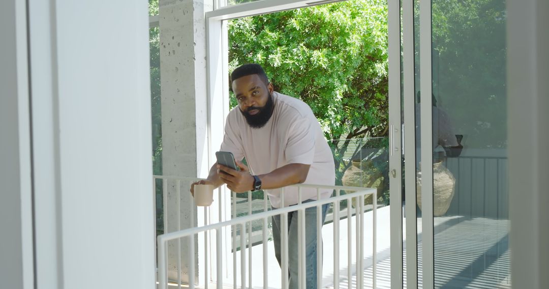 Man Relaxing on Balcony Checking Smartphone and Holding Coffee Mug